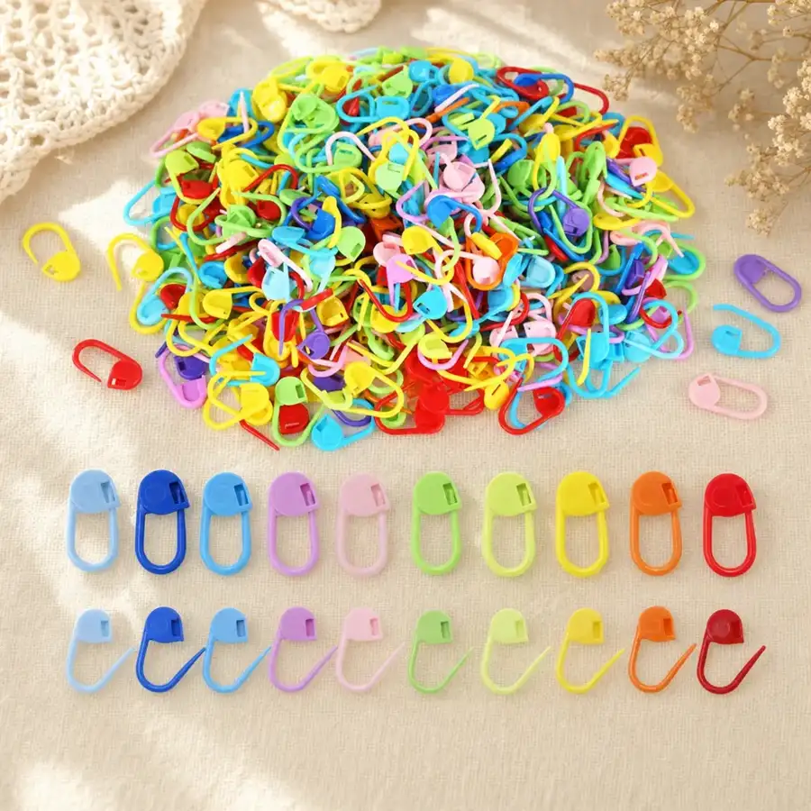 Flat lay of the Stitchling 50-pack: pile of assorted color locking stitch markers on warm linen