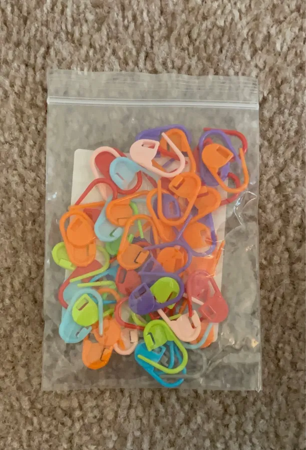 Buyer photo of assorted color stitch markers spread on a wooden table